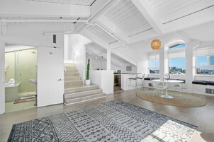 Un interior moderno con una escalera que lleva a una zona de cocina, un comedor con mesa redonda y vistas de la ciudad a través de amplios ventanales.