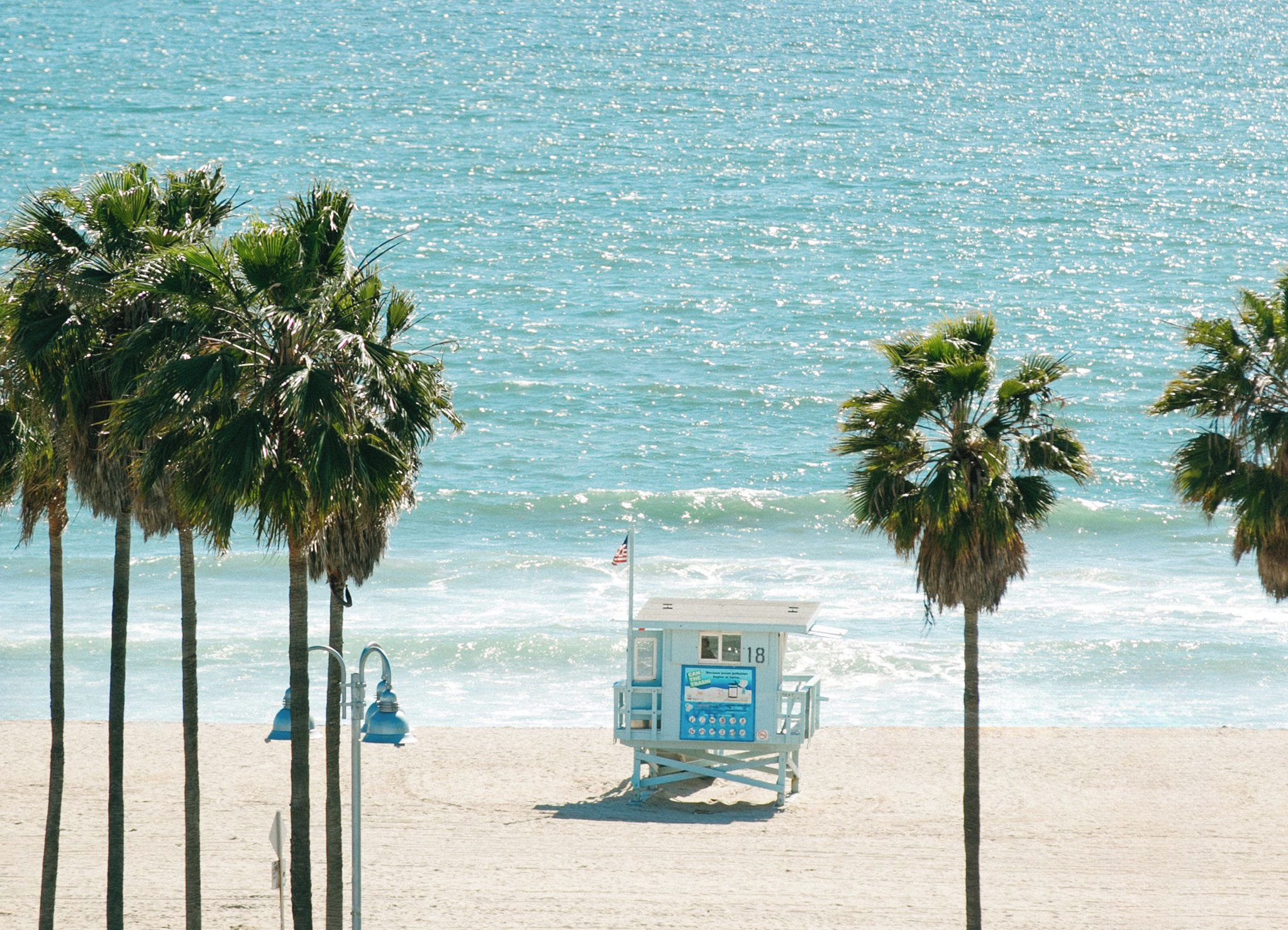 A lifeguard tower on a sandy beach with palm trees and ocean waves in the background.
