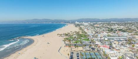 Un paisaje urbano costero con playa, canchas de tenis y edificios residenciales.