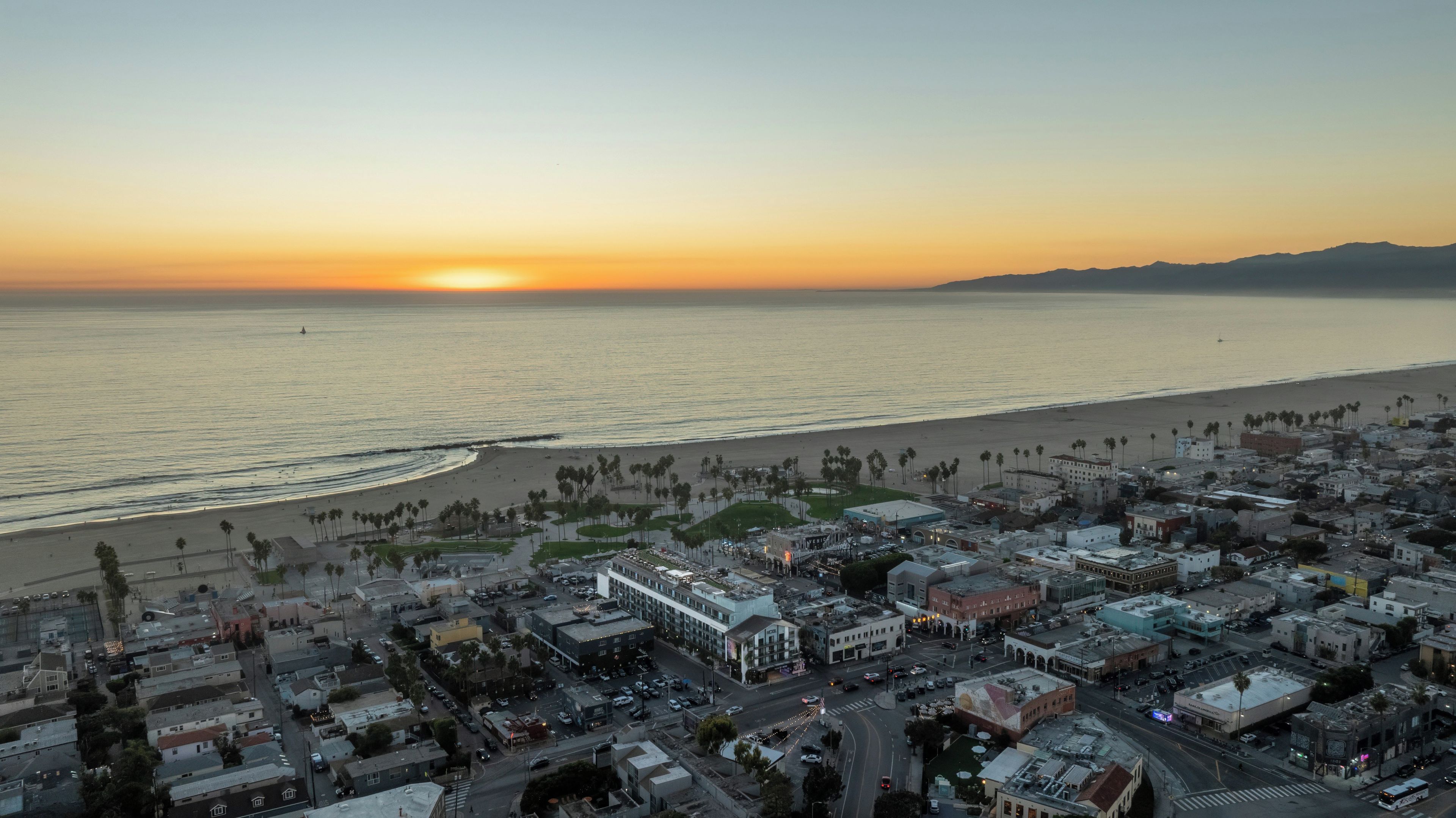 Un paysage urbain côtier avec une plage, des bâtiments et un coucher de soleil.