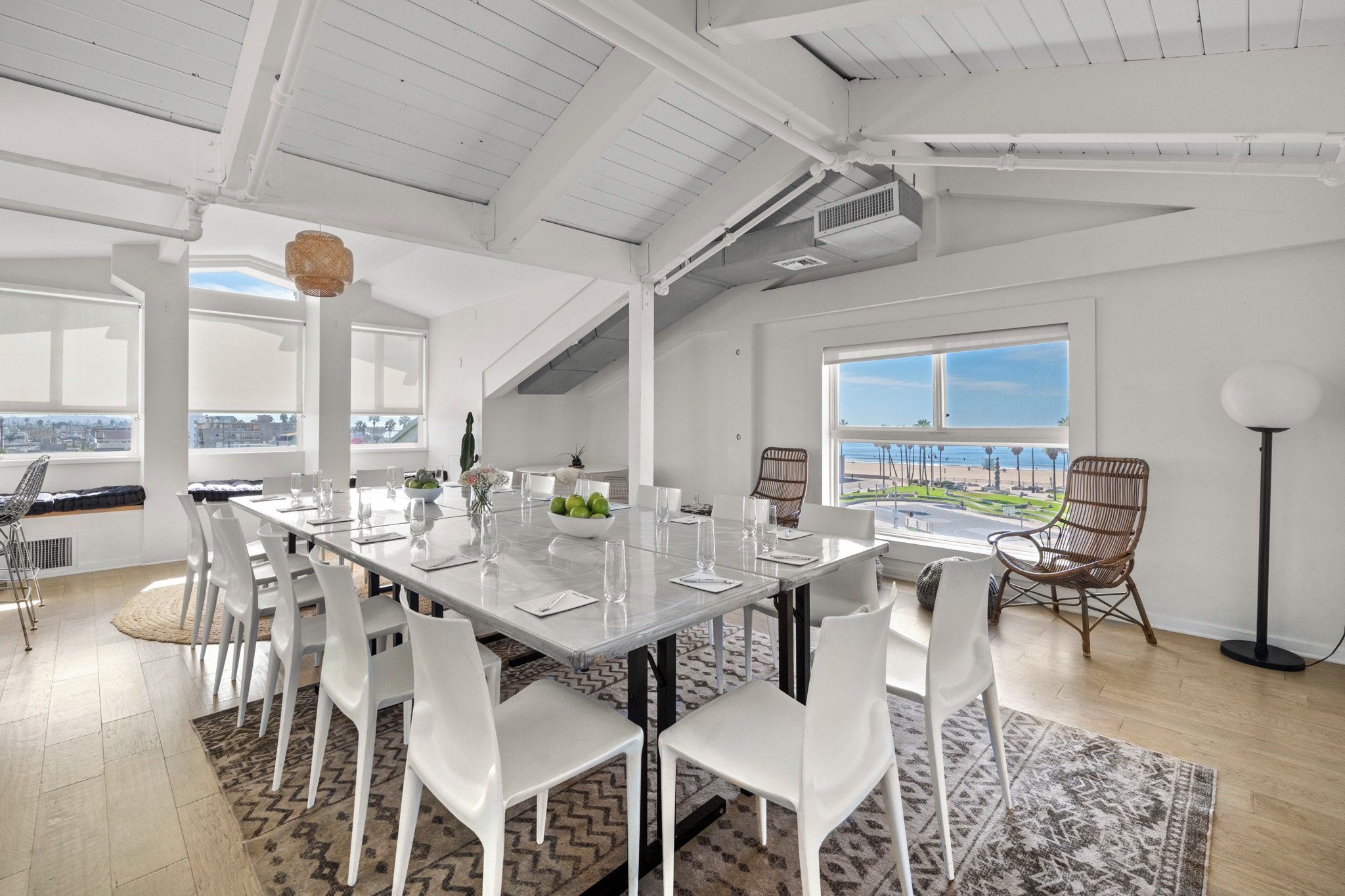 A spacious dining area with a long table, white chairs, and a view of the beach.