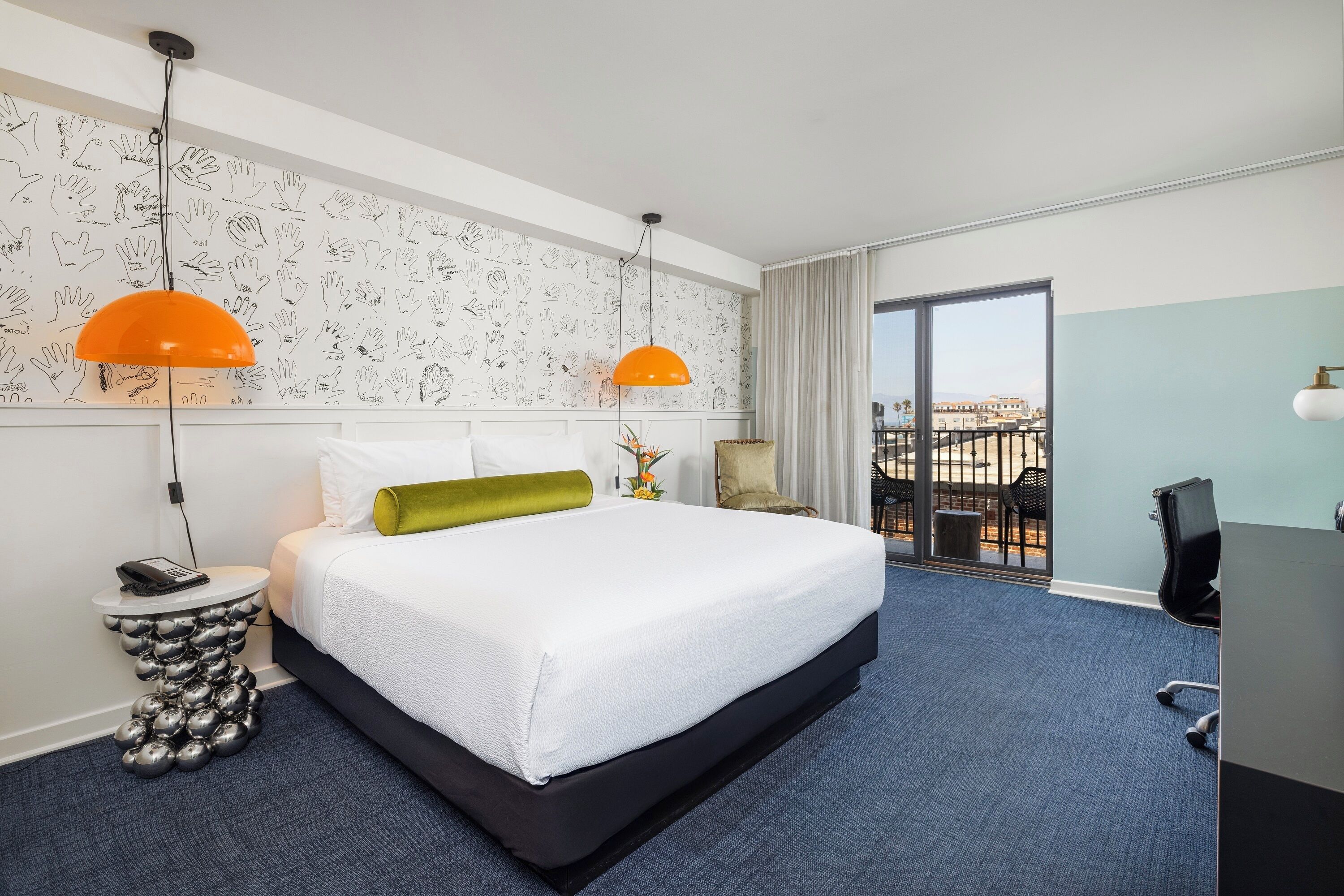 Une chambre d’hôtel avec un grand lit, deux lampes suspendues, un bureau et une vue sur la ville.