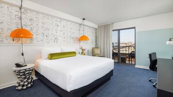 Une chambre d’hôtel avec un grand lit, deux lampes suspendues, un bureau et une vue sur la ville.