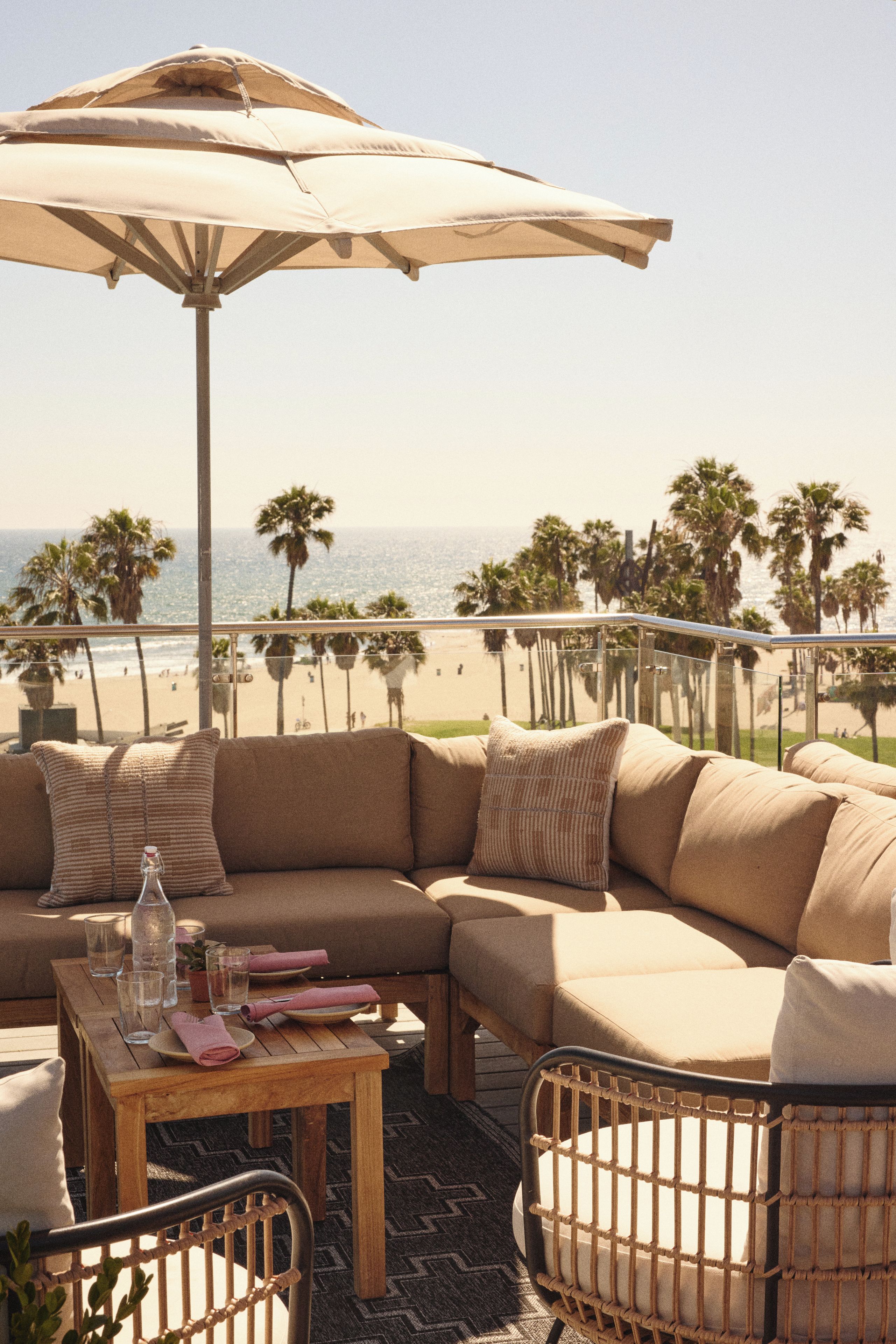 A beachside seating area with a large umbrella, a wooden table, and a wicker chair.