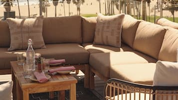 A beachside seating area with a large umbrella, a wooden table, and a wicker chair.