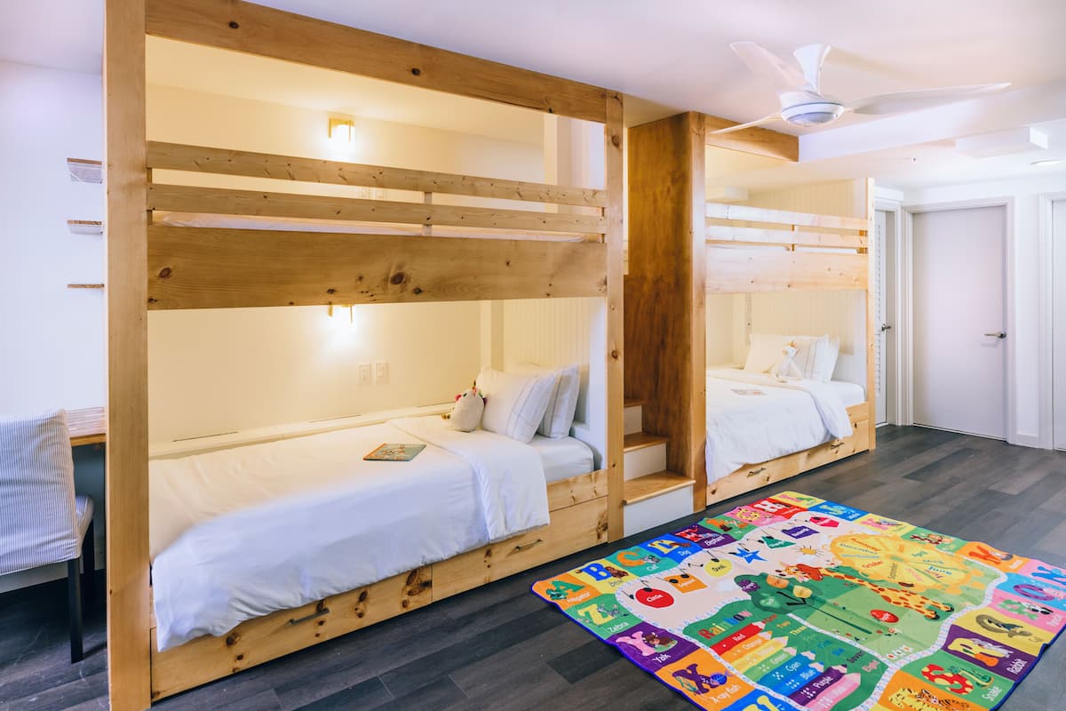 A room with two bunk beds, a ceiling fan, and a colorful alphabet-themed rug.