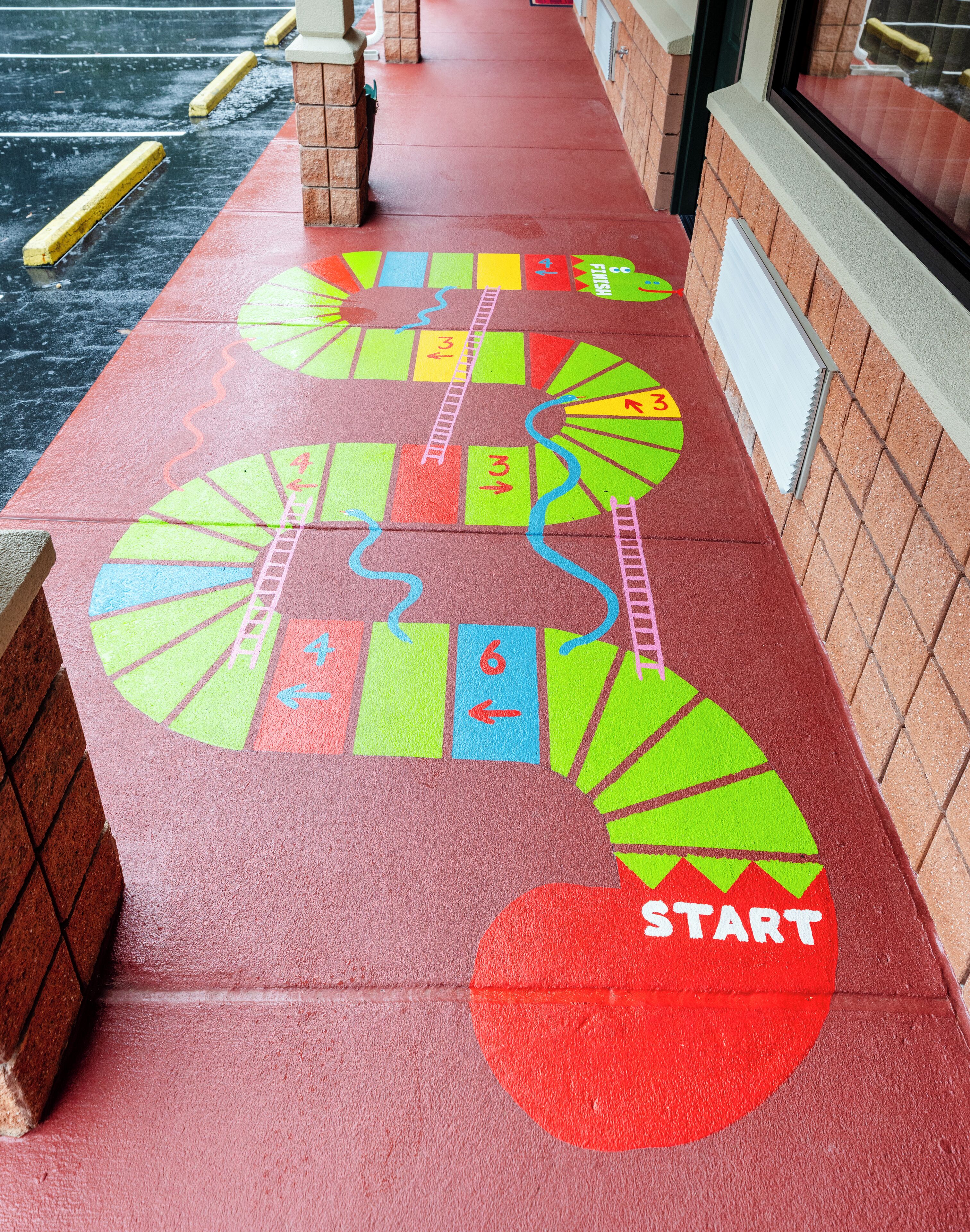 Un camino de juego de mesa colorido sobre pavimento mojado, con un punto de partida marcado por un círculo rojo.