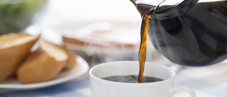 A cup of coffee being poured from a black coffee pot onto a white saucer.