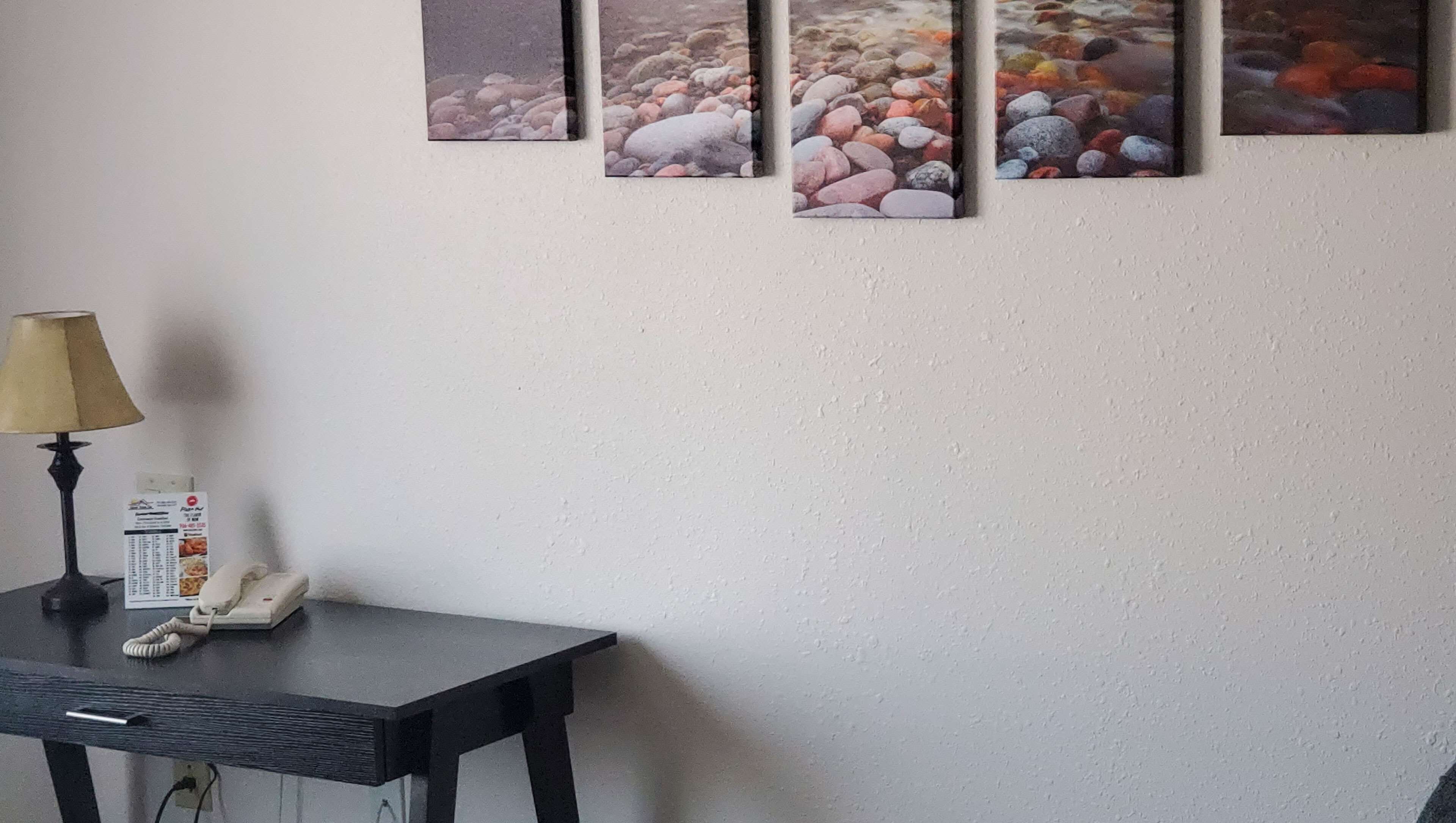 A room with a table, a lamp, a phone, and a wall with four framed pictures.