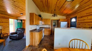 A cabin interior with a dining area, kitchen, and a living space with a fireplace.