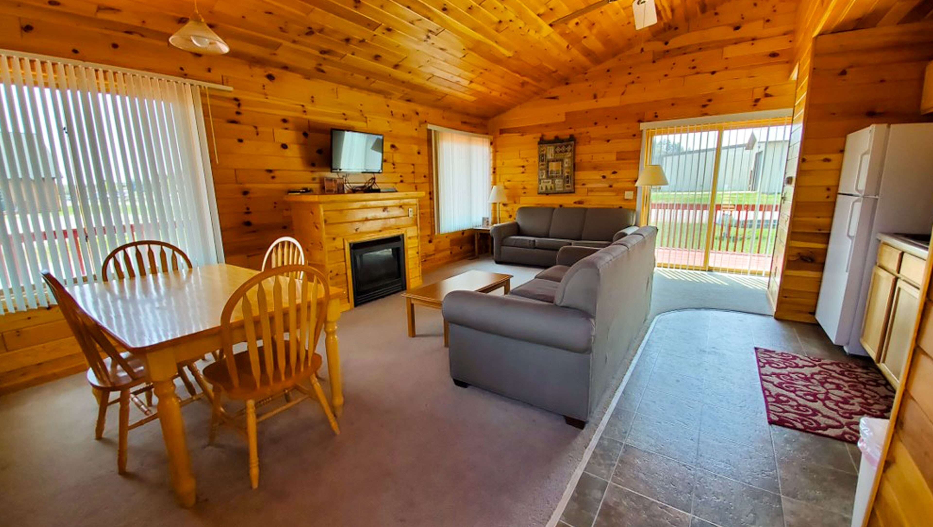 L'intérieur d'un chalet en bois comprend une table à manger, des chaises, un canapé, un téléviseur et une cheminée.