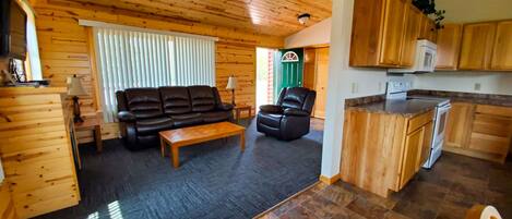 L’intérieur chaleureux d’un chalet comprend un espace de vie avec un canapé et un fauteuil inclinable, une table à manger en bois et une cuisine dotée de meubles en bois et d’un plan de travail.