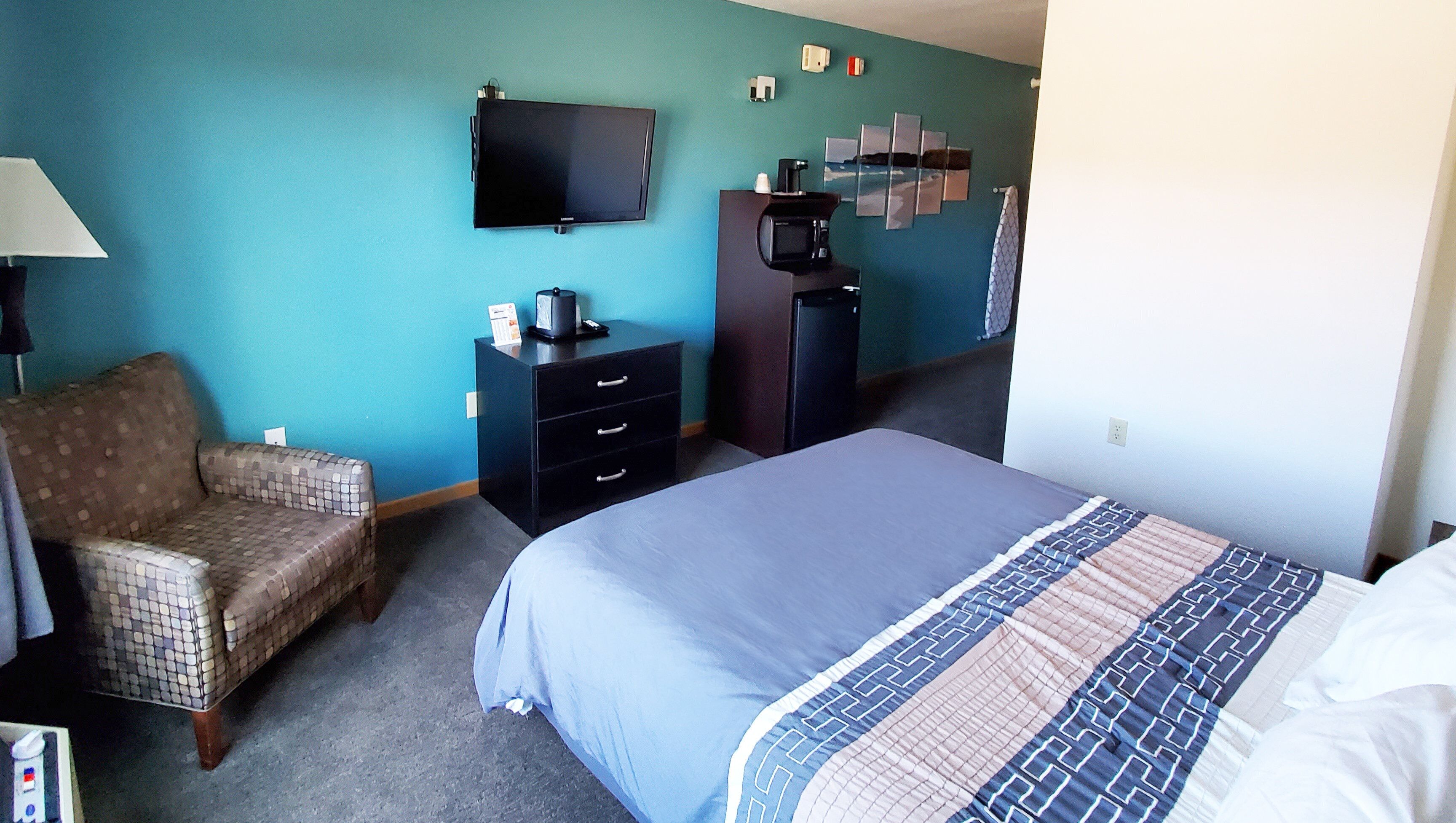 A hotel room with a bed, a chair, a dresser, a television, and a coffee maker.