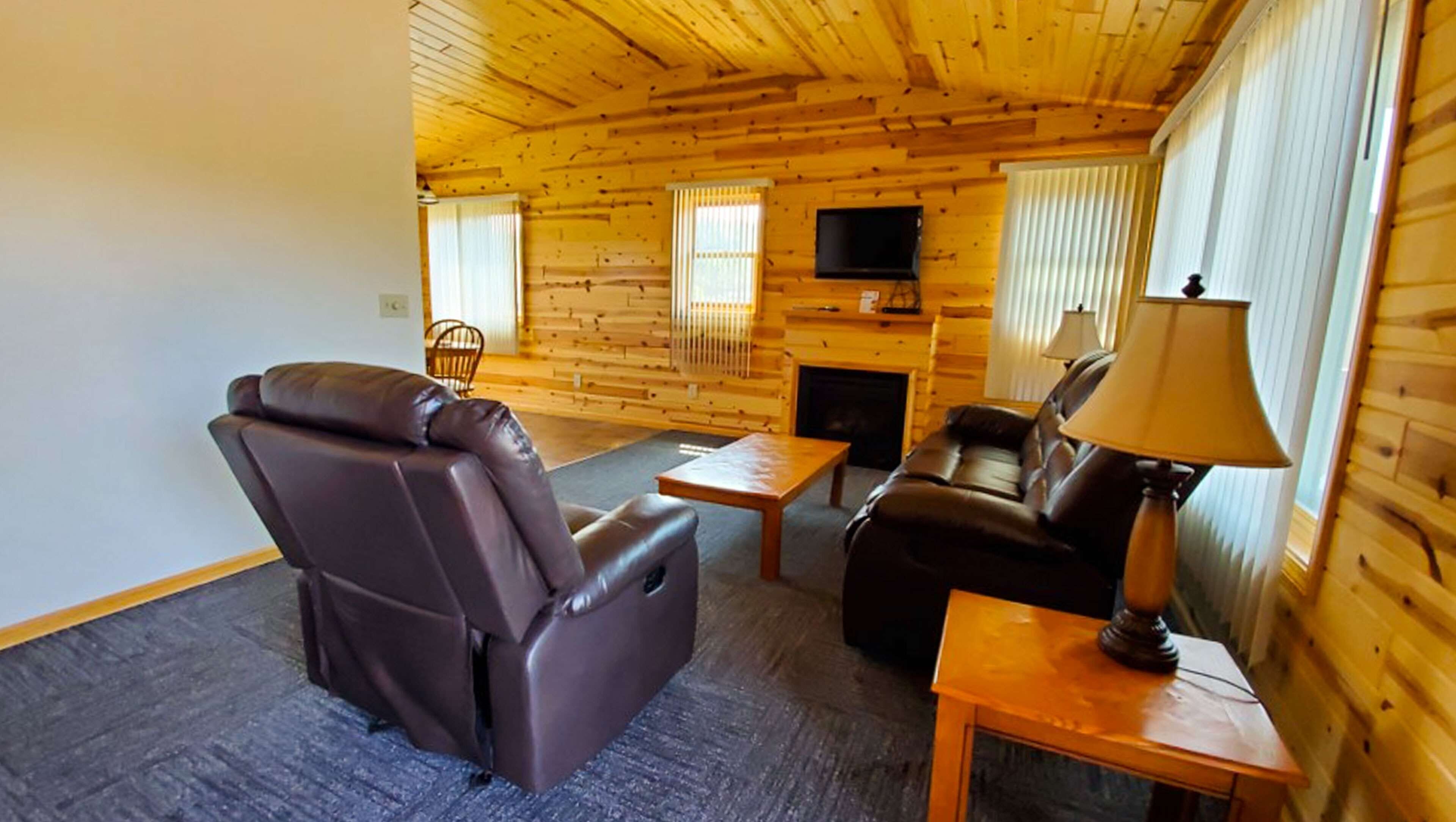 Ein Blockhaus-Interieur mit Ledersessel, Sofa, einem kleinen Tisch und einer Lampe.