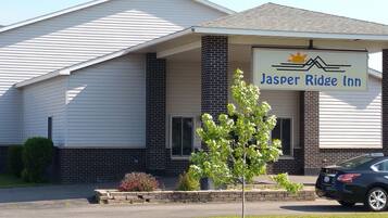 Un motel appelé Jasper Ridge Inn, avec une façade simple, une entrée abritée et un espace de stationnement où se trouve une voiture.