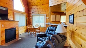 A cozy cabin interior with a fireplace, a dining area, and a living room with a sofa and a lamp. - Jasper Ridge Inn Ishpeming (Ishpeming)