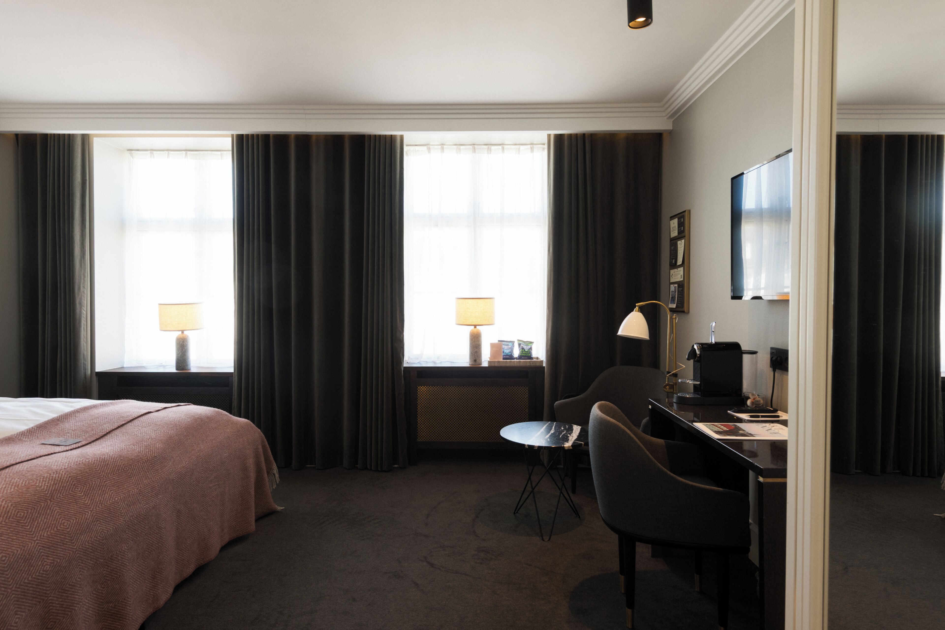 A hotel room with a bed, desk, chair, lamp, and a television.