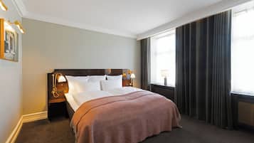 Habitación de hotel con una cama grande, una mesita de noche con lámpara, una ventana con cortinas y un cuadro colgado en la pared.