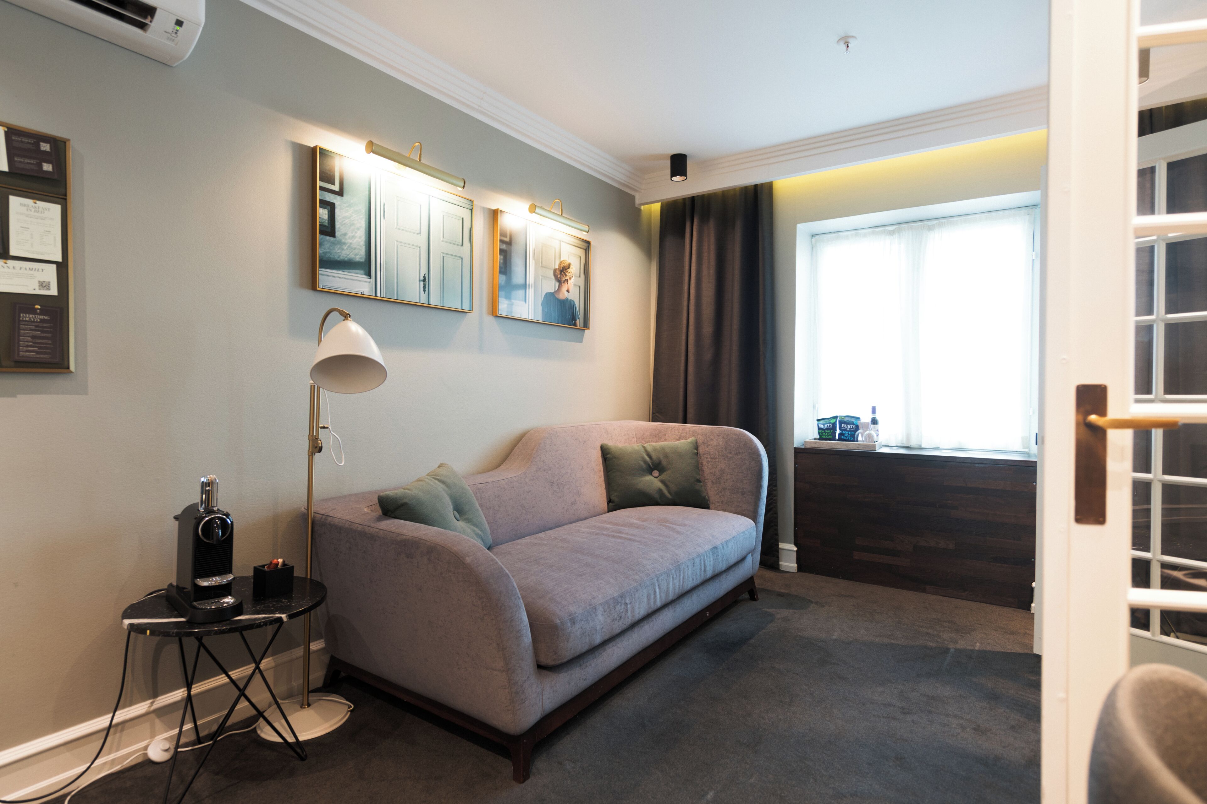 Un salon moderne avec un canapé, une table d’appoint, une lampe et une fenêtre avec des rideaux.