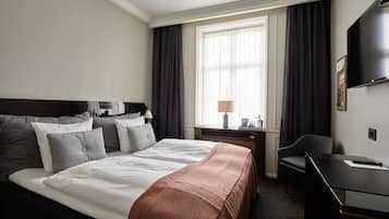 Habitación de hotel con una cama grande, un escritorio, una silla, un televisor y una ventana con cortinas.