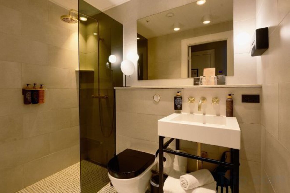 Un baño moderno con ducha envuelta en vidrio, un lavabo blanco y un inodoro negro.