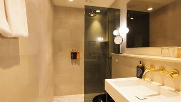 A modern bathroom with a glass shower enclosure, a white sink with gold fixtures, and a mirror with lights.