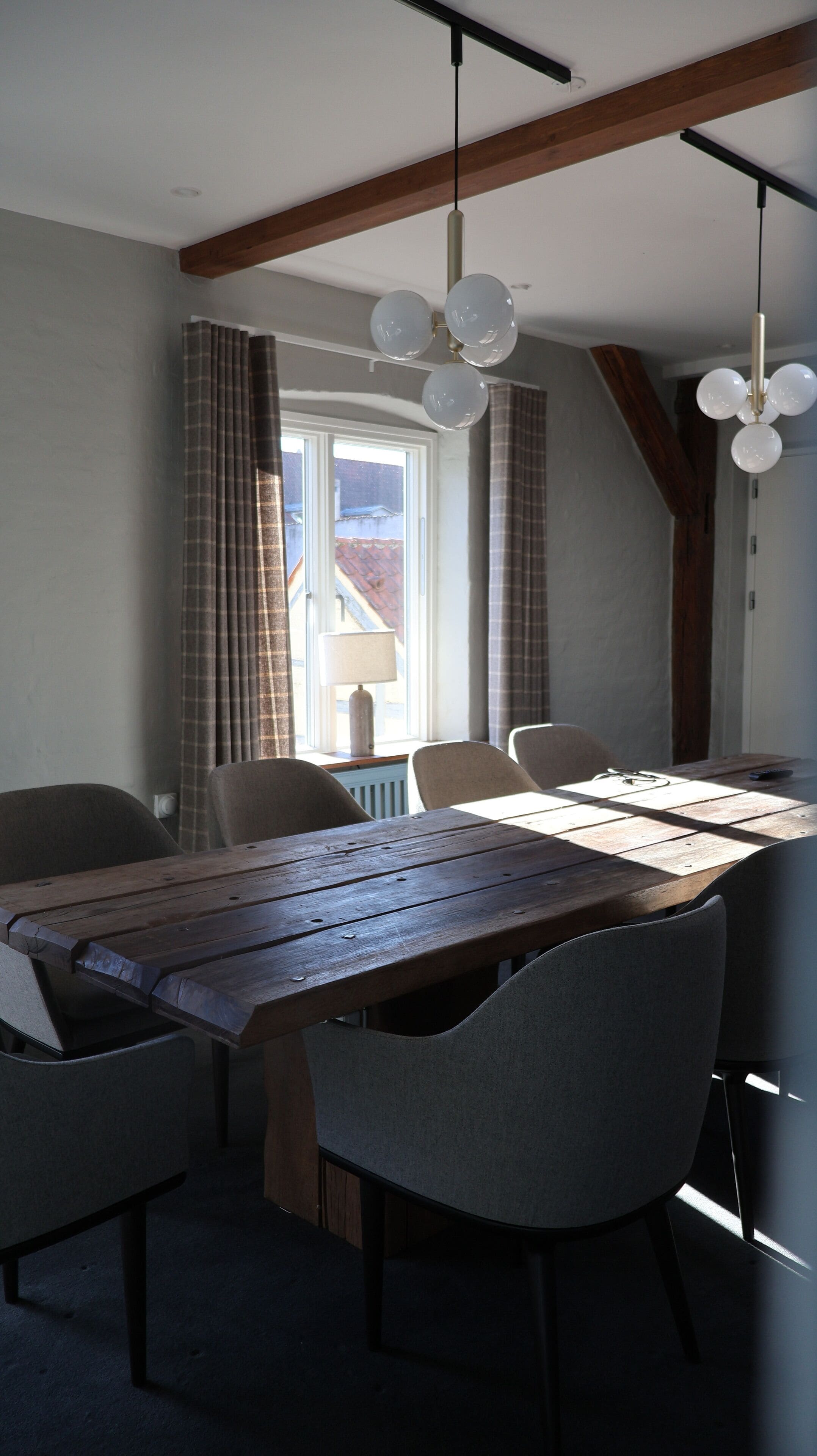 Ein Essbereich mit Holztisch, grau gepolsterten Stühlen und Pendelleuchten.