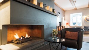 A fireplace with logs, a vase with flowers, and a chair in a room with a blue wall and wooden beams. - Hotel SKT. Annæ (Copenhagen)