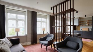 A modern living room with a sofa, two armchairs, a coffee table, and a kitchen area with cabinets and a dining table. - Hotel SKT. Annæ (Copenhagen)