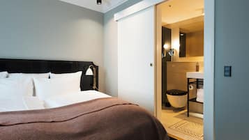 Une chambre d’hôtel comprenant un lit, une table de chevet, une lampe, une salle de bain avec des toilettes, un lavabo et un miroir.