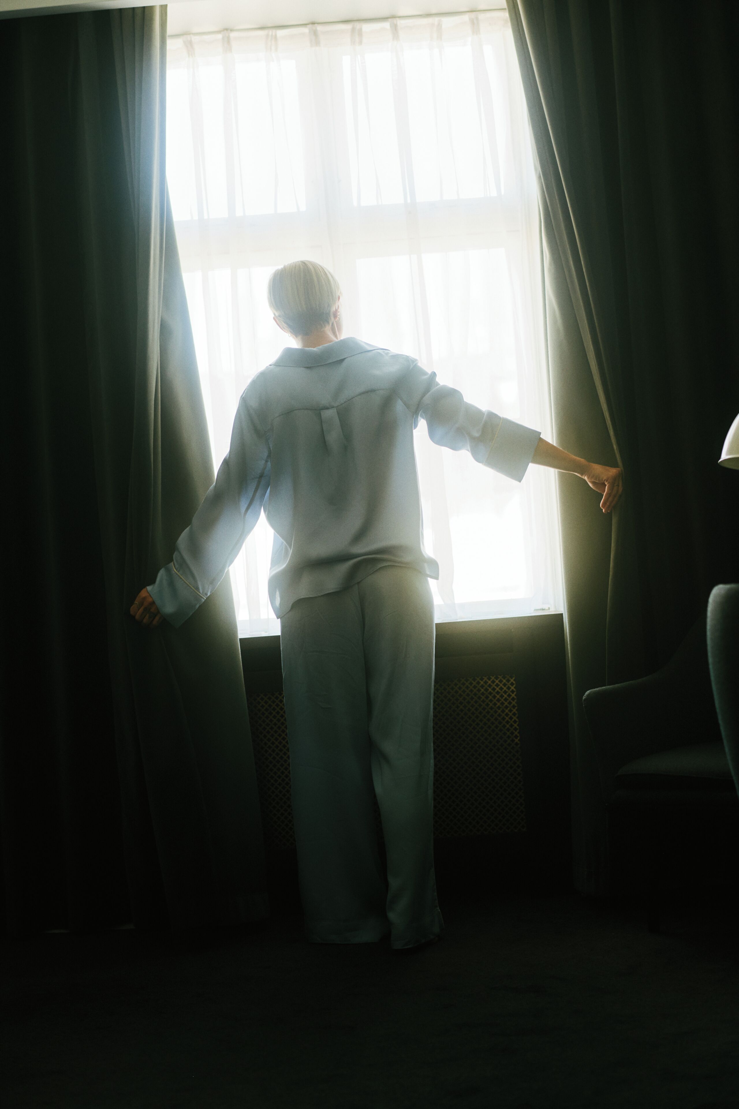 Una persona de espaldas, de pie junto a una ventana con cortinas.