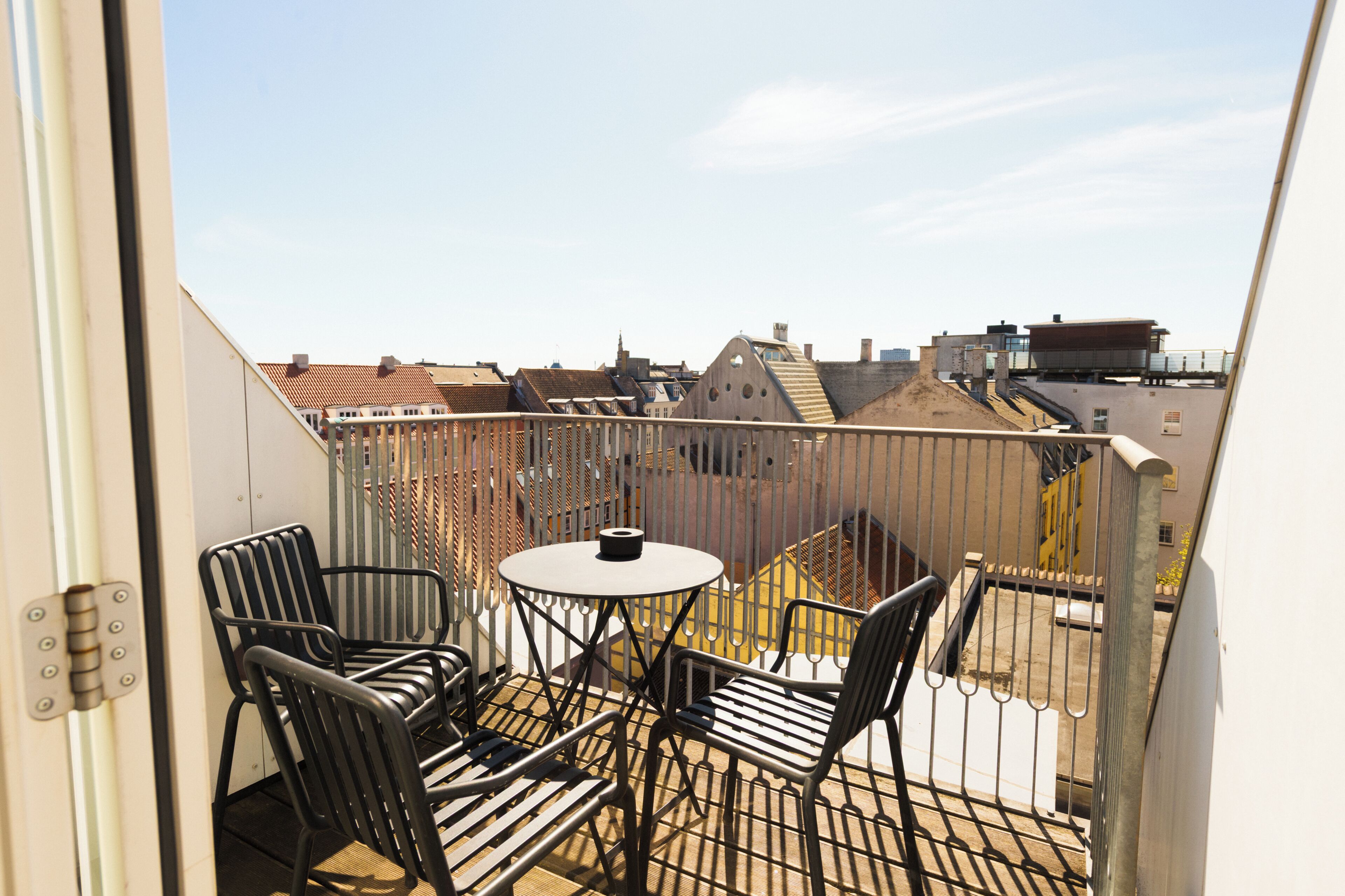 A balcony with a table and chairs, a view of the cityscape, and a metal railing.