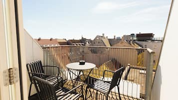 A balcony with a table and chairs, a view of the cityscape, and a metal railing.