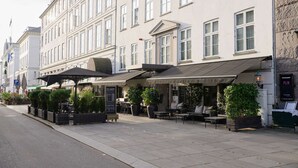 A row of outdoor seating areas with tables and chairs, a signboard, and potted plants. - Hotel SKT. Annæ (Copenhagen)