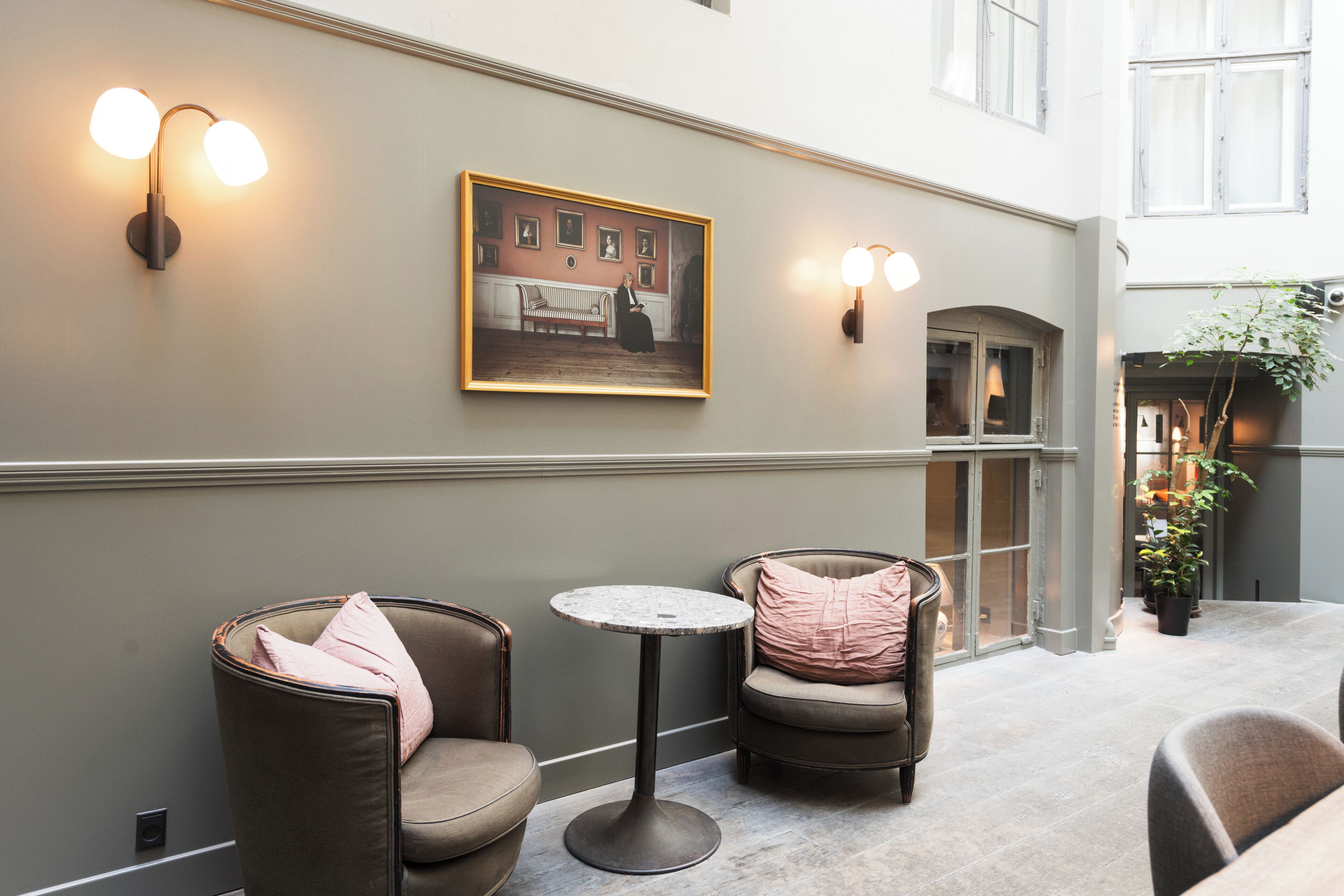A hallway with two cushioned chairs, a small round table, and a framed picture on the wall.