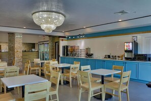 Restaurante com mesas e cadeiras de madeira, balcão azul com máquina de café e um lustre.