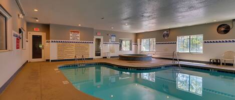 Une piscine intérieure à l’eau claire, un jacuzzi et un espace détente avec des fauteuils.