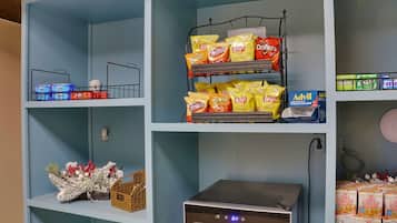A kitchen with a microwave, a coffee maker, and shelves with snacks and beverages.