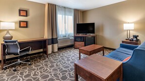 A hotel room with a desk, chair, TV, sofa, and two lamps. - Comfort Inn Dyersville Near Field of Dreams (Dyersville)