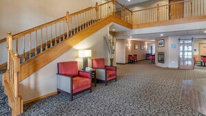 A hotel lobby with a wooden staircase, red armchairs, a patterned carpet, and a seating area with tables. - Comfort Inn Dyersville Near Field of Dreams (Dyersville)