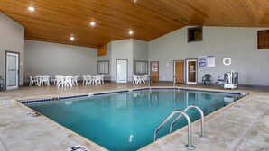 An indoor swimming pool with a 4'6" depth sign, surrounded by white chairs and tables, wooden ceiling, and signs indicating no diving and chemical water treatment. - Comfort Inn Dyersville Near Field of Dreams (Dyersville)
