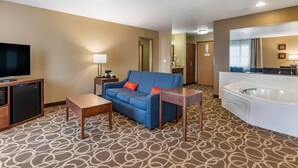 A hotel room with a sofa, a small table, a TV, a mini-fridge, a bathroom with a bathtub, and a patterned carpet. - Comfort Inn Dyersville Near Field of Dreams (Dyersville)