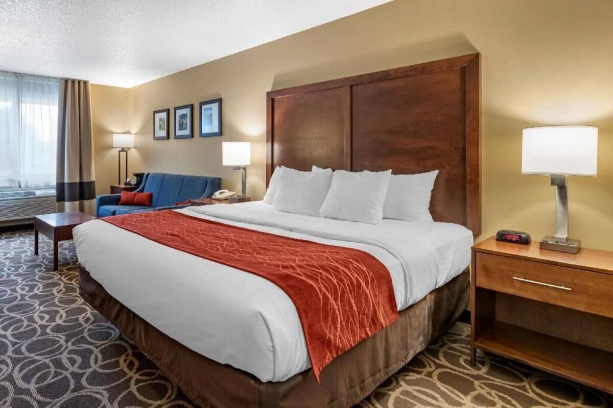 A hotel room with a large bed, a desk, a chair, and a lamp.
