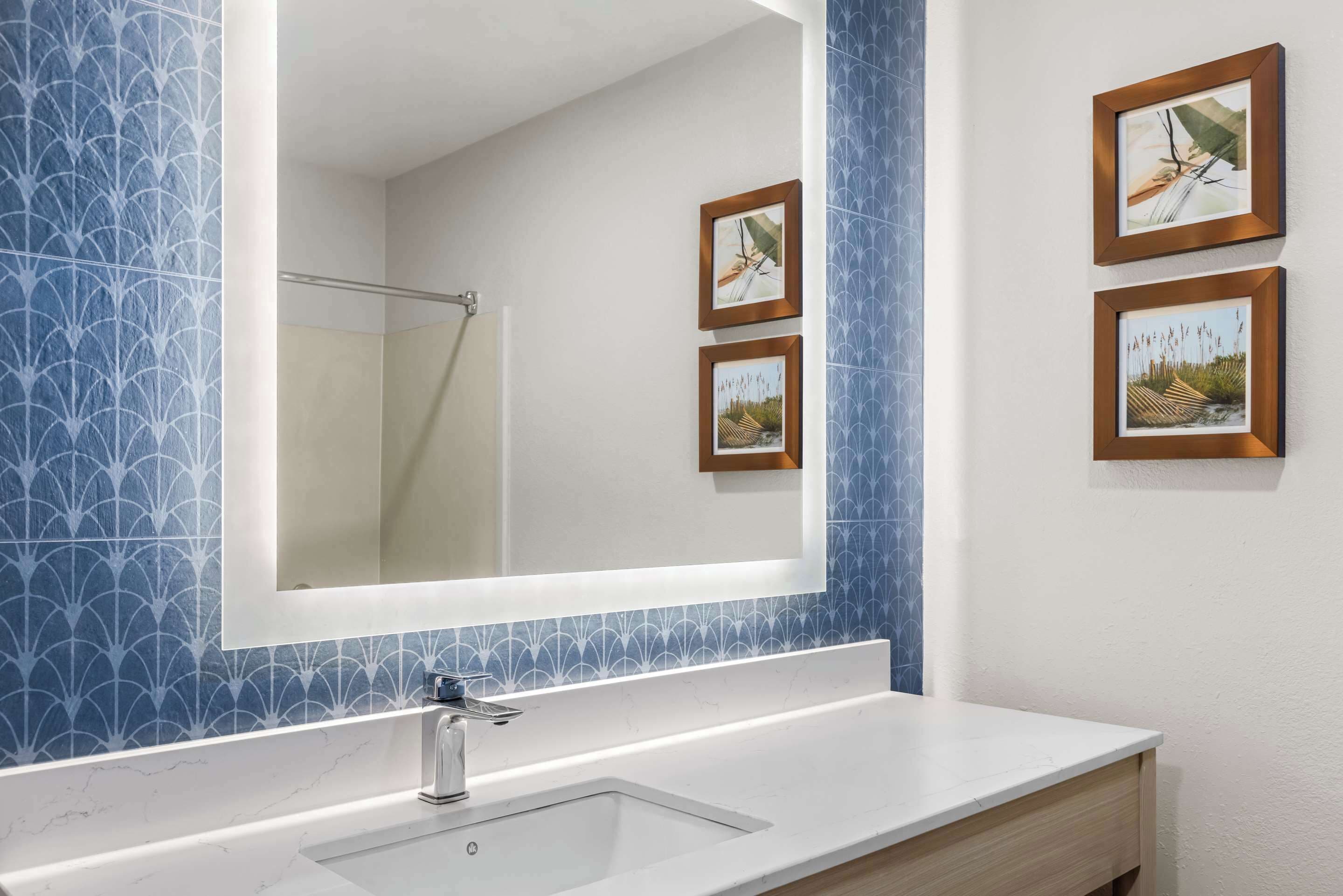 A bathroom with a large mirror, a white sink, and three framed pictures on the wall.