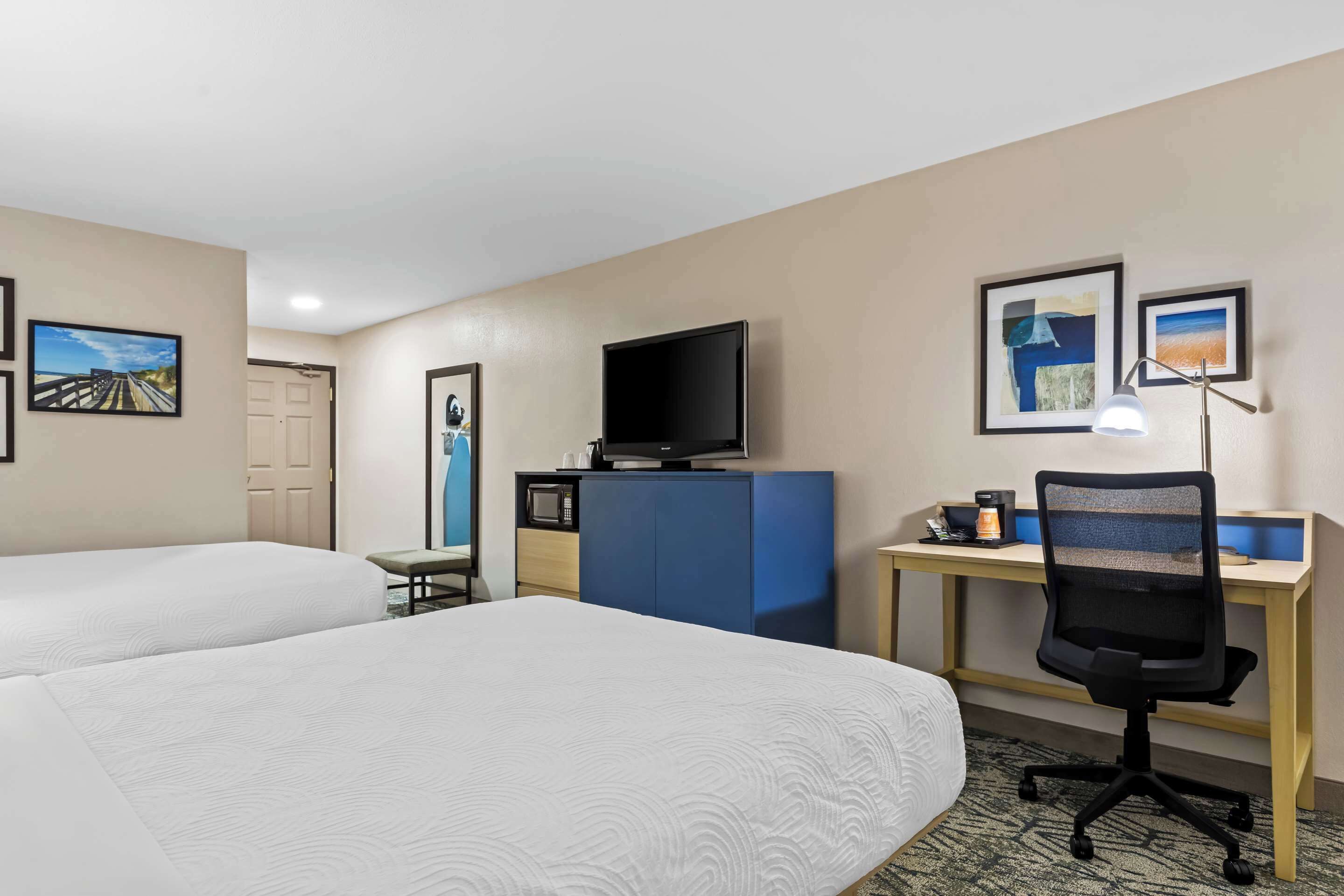 Habitación de hotel con dos camas, un escritorio con computadora, televisor y una silla.