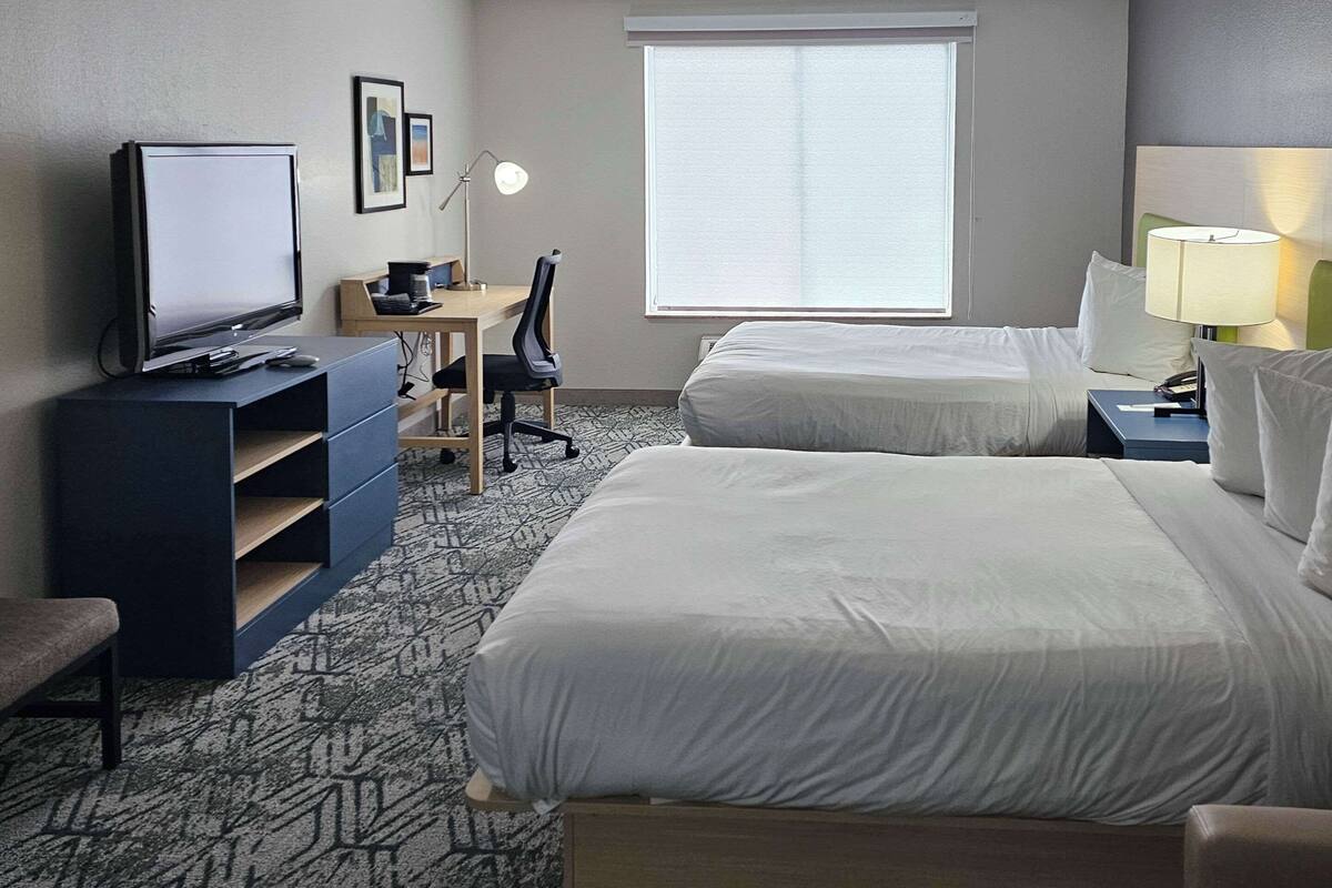 Habitación de hotel con dos camas, un escritorio, una computadora, un televisor y una lámpara.