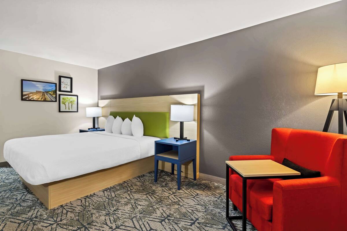 Una habitación de hotel con cama, escritorio, silla y mesita de noche.