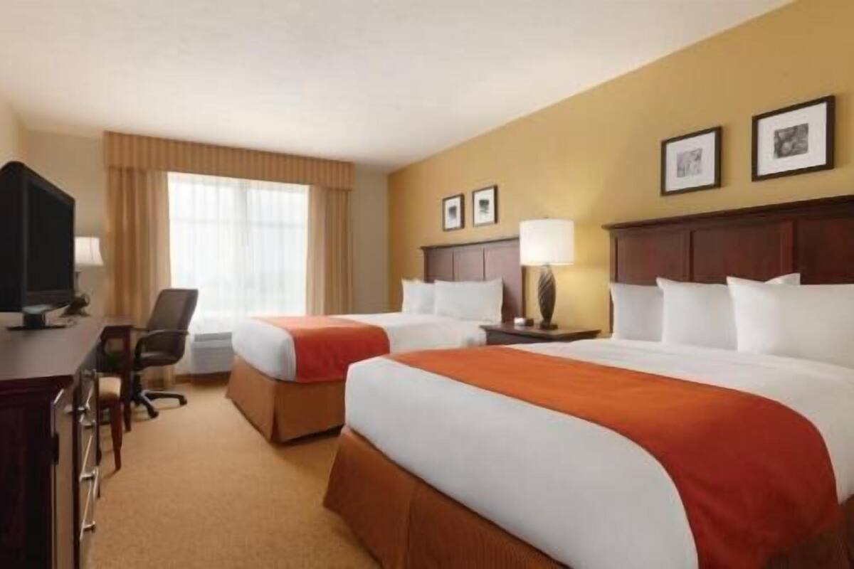 Habitación de hotel con dos camas, un escritorio con computadora, una silla y un ventanal con cortinas.
