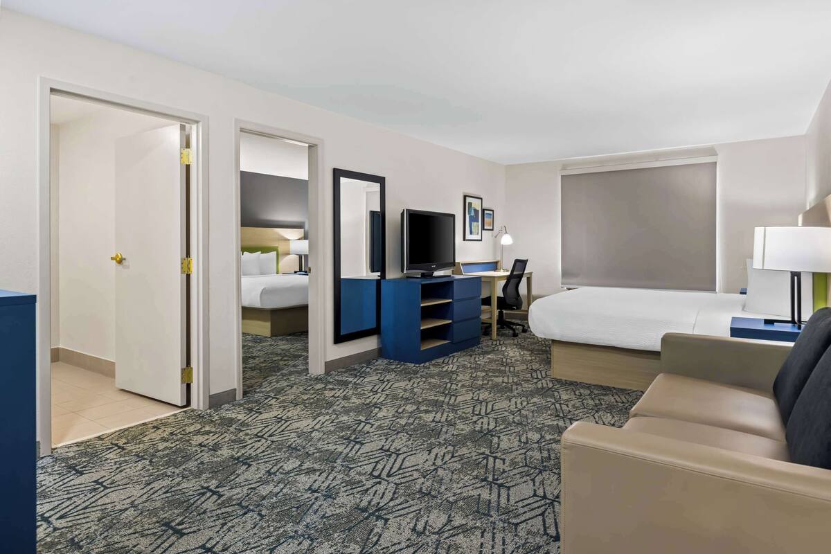 Habitación de hotel con cama, escritorio con computadora, televisión y zona de estar con sofá.