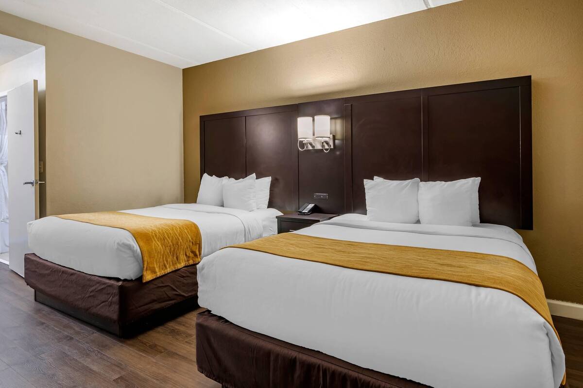 A hotel room with two beds, a large dark headboard, a bedside table with a phone, and a door leading to a bathroom.